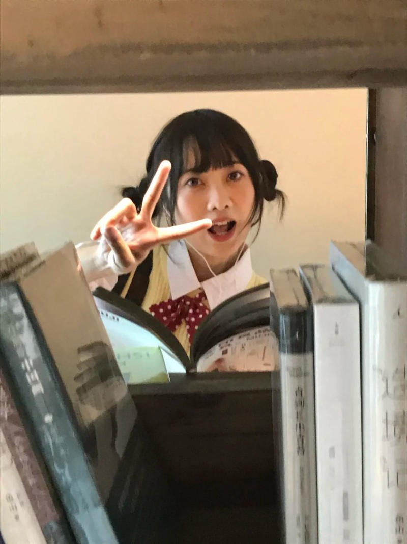 (lấp ló sau hàng sách, biểu cảm vui tươi)