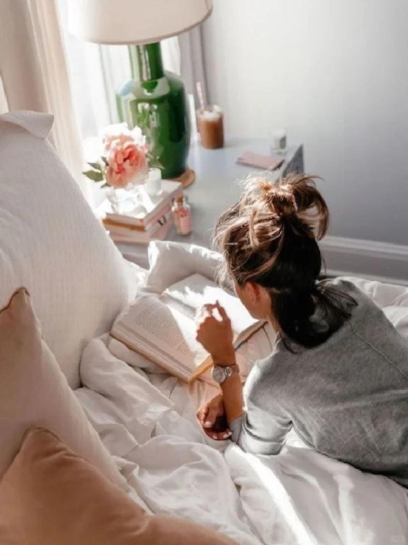 (nằm sấp, sách đặt trên giường, chụp từ phía sau)