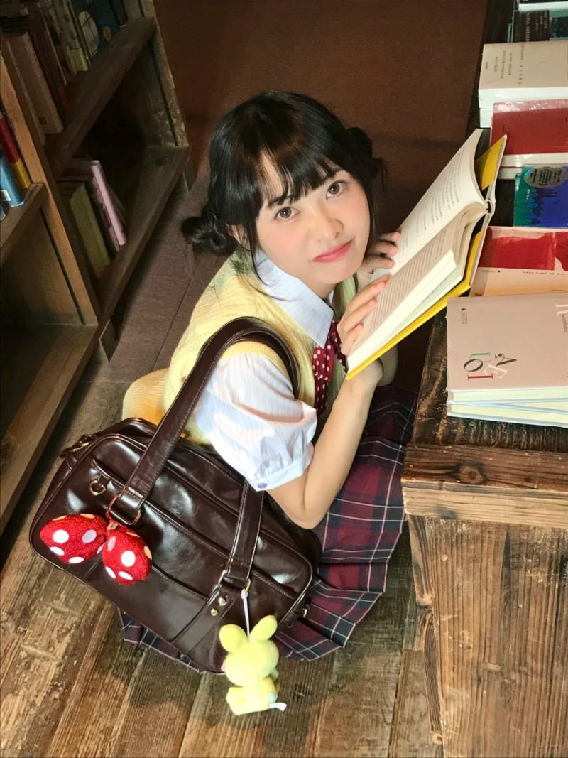 (chụp từ trên xuống, tay cầm sách mở, mắt nhìn thẳng ống kính)