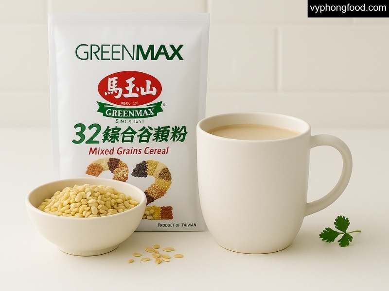 Ly bột ngũ cốc dinh dưỡng GREENMAX Đài Loan pha nóng trên bàn bếp sạch, cạnh bát hạt ngũ cốc.