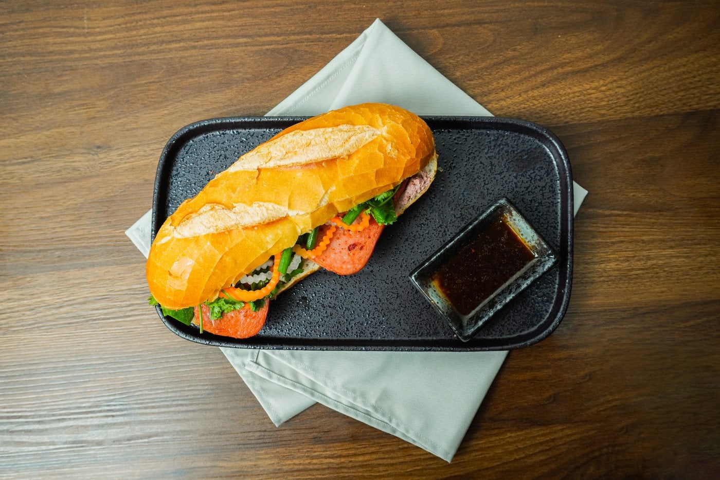 Bánh mì thịt hộp Tulip nướng ngũ vị trên khay đá, ăn kèm chén sốt nước tương ngũ vị