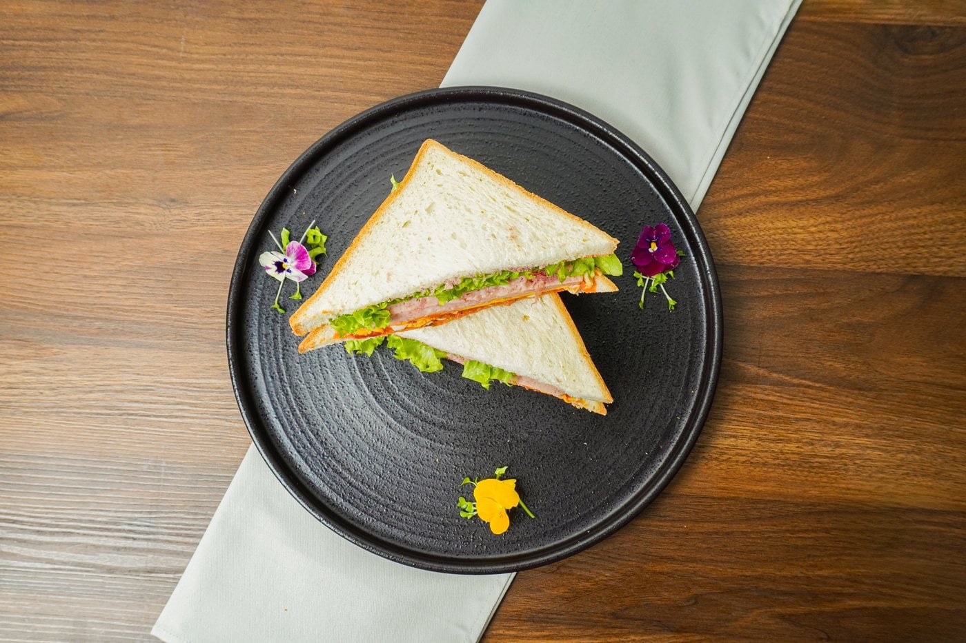 Sandwich thịt hộp Tulip trứng vàng áp chảo cắt đôi, bày trên đĩa gốm đen