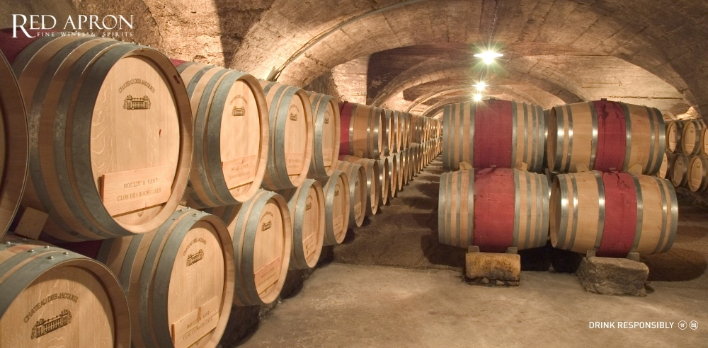 Hầm rượu vang Maison Louis Jadot với các thùng gỗ sồi Pháp xếp dọc, minh họa quy trình ủ rượu vang Burgundy cao cấp được Red Apron phân phối.