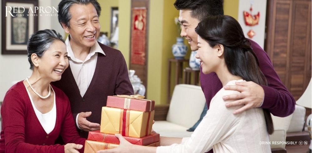 Gia đình trao hộp quà Tết màu đỏ vàng cho bố mẹ trong phòng khách, thể hiện lòng hiếu thảo dịp Tết.