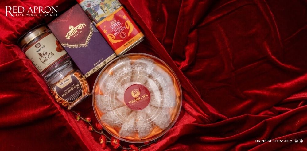 Hộp quà sức khỏe gồm hộp saffron, hũ sản phẩm dinh dưỡng và hũ yến trên nền đỏ, gợi ý quà Tết cho bố mẹ.