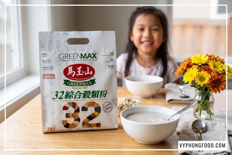 Ly bột ngũ cốc cho người gầy không đường Greenmax Đài Loan sánh mịn thơm bùi đặt cạnh túi sản phẩm và bát hoa quả trên bàn gỗ sồi ngập tràn ánh nắng buổi sáng ấm áp giúp bồi bổ sức khỏe an toàn tại VyPhongFood.