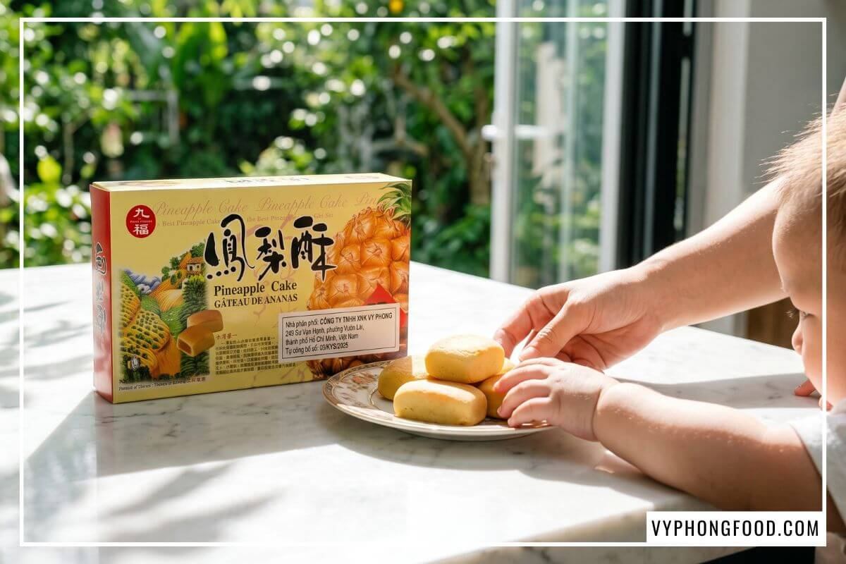 Bé háo hức vươn tay lấy chiếc bánh trên bàn đá cạnh hộp bánh dứa Nice Choice dán tem phụ Vy Phong Food.