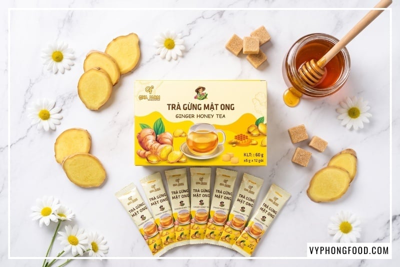 Bố cục flatlay nghệ thuật của hộp trà gừng mật ong gói QNA Farm hòa tan cùng các lát gừng sẻ Tiên Phước và mật ong rừng nguyên chất, minh họa cho công thức trà gừng sạch lành thuận tự nhiên.
