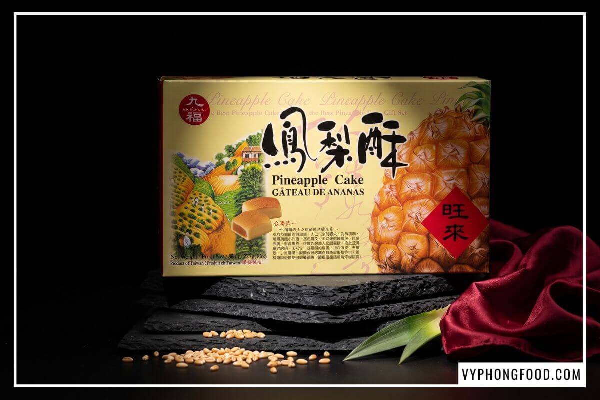 Hộp bánh dứa Đài Loan Nice Choice 227g màu vàng cam đặt nghiêng trên bục đá đen nhiều tầng cùng bông lúa mì.