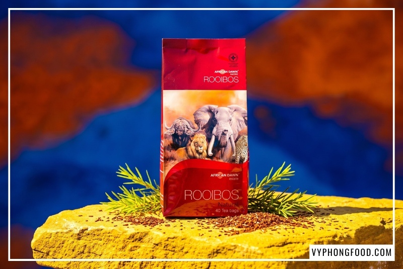 Bao bì sản phẩm trà đỏ Nam Phi pha chế nhãn hiệu African Dawn đặt nổi bật trên phiến đá vàng giữa thiên nhiên Cederberg Nam Phi do Vy Phong Food phân phối.