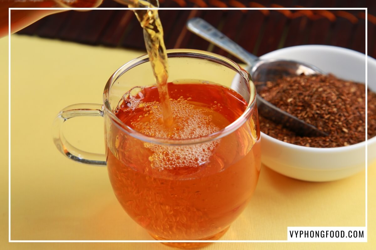 Chén gốm trà rooibos đỏ đất và lá trà khô rải trên phiến đá sa thạch Nam Phi