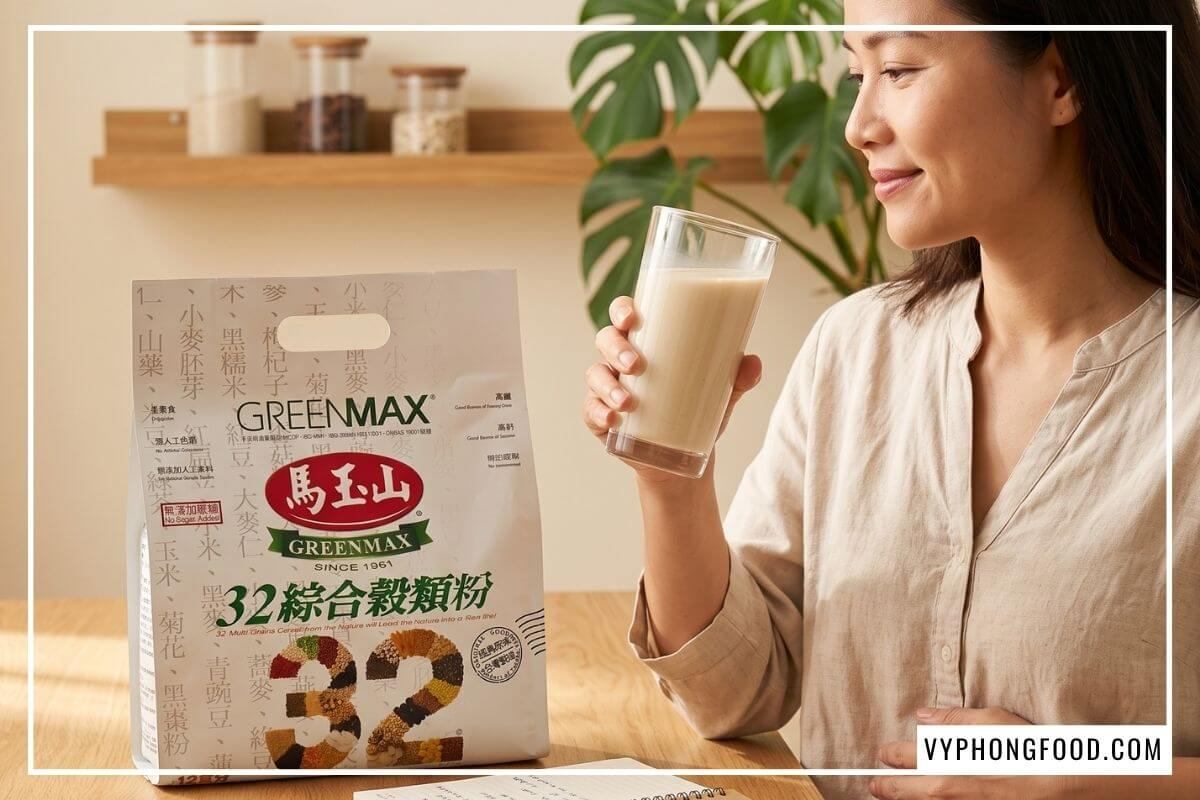 Người phụ nữ nâng ly thủy tinh bột ngũ cốc 32 loại hạt Greenmax sánh mịn bên bàn gỗ sồi chuẩn thực phẩm chay an toàn