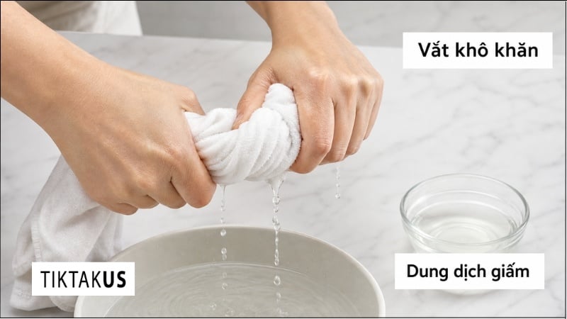 Thao tác vắt kiệt khăn ẩm đã nhúng qua dung dịch giấm trắng pha loãng trước khi lau dây da