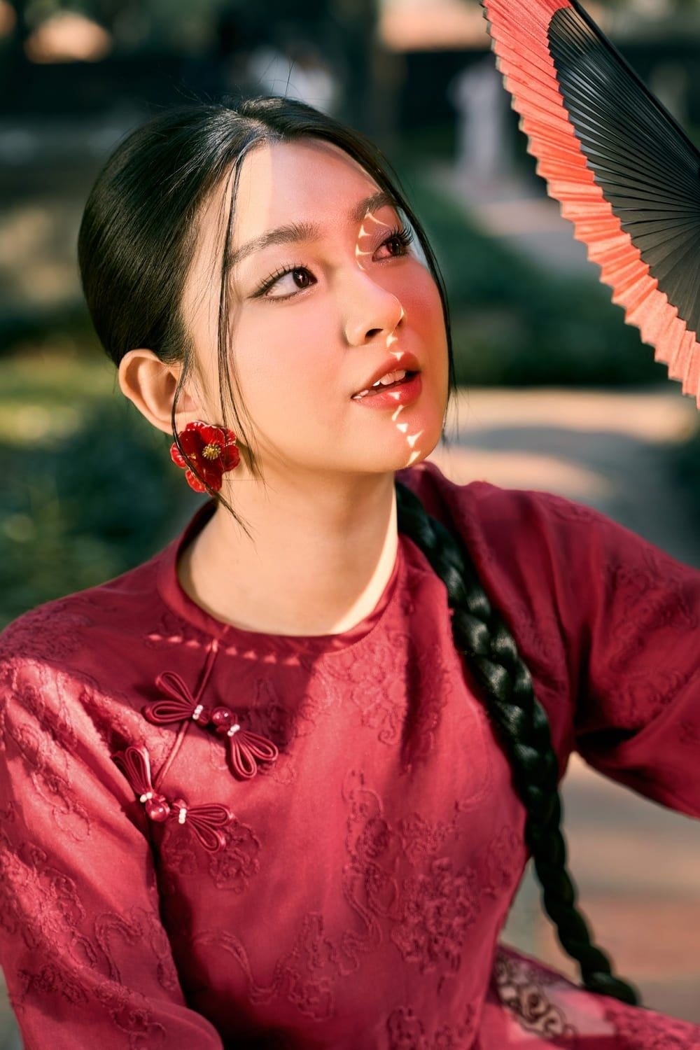 Ngẩng đầu đón nắng, tay cầm quạt che một phần mặt, mắt nhìn lên trên, góc chụp cận mặt