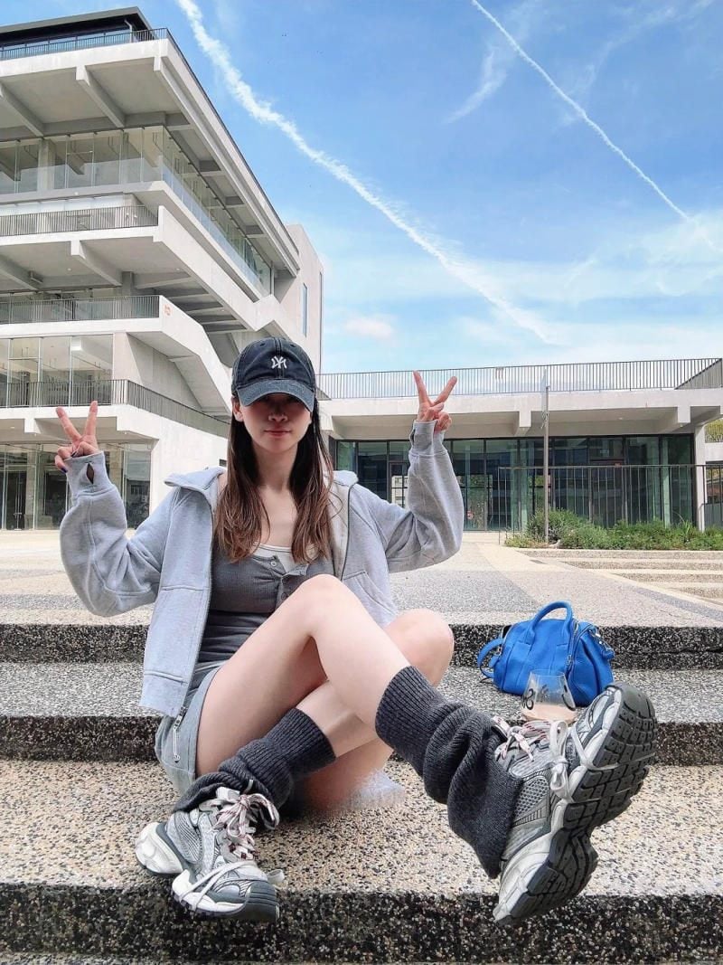 7. Áo khoác hoodie xám + váy ngắn + tất ống chân (leg warmers) + giày Balenciaga Triple S lưới