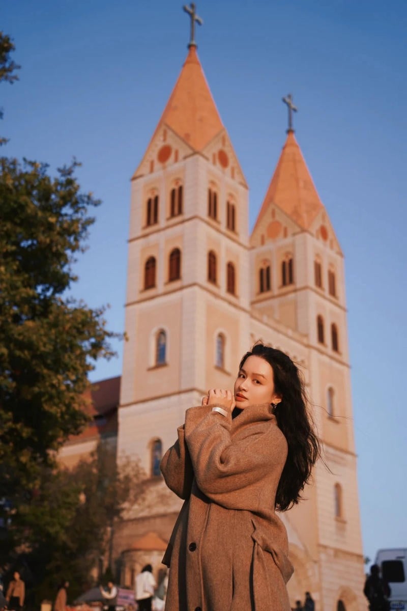 Đứng ngoài trời, hai tay đan nhẹ dưới cằm, gió thổi tóc bay