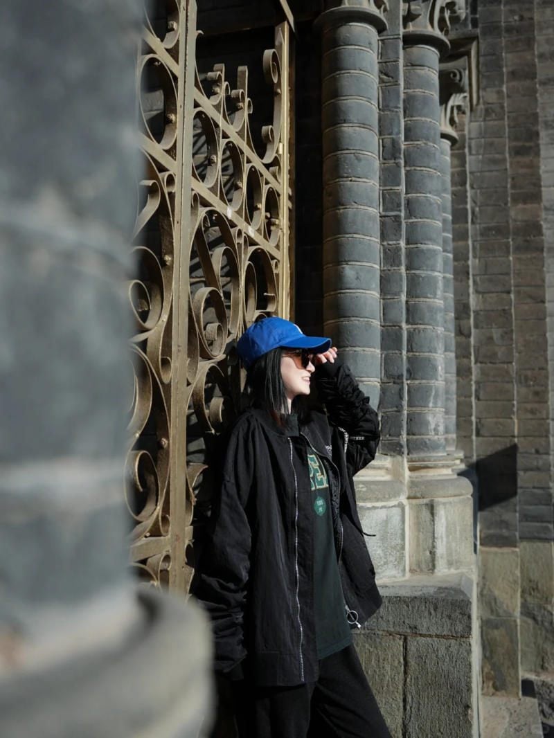 Tựa lưng vào cổng, tay chỉnh mũ cười tươi