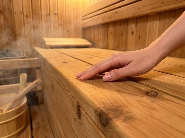 Bàn tay chạm vào bề mặt gỗ thông nhẵn mịn, cảm nhận sự cao cấp của phòng xông hơi.