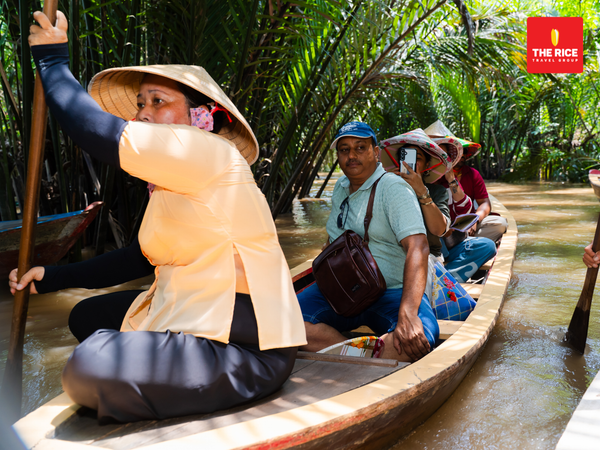 Guests on The Rice Travel Group's Mekong Delta tour drift beneath cool water coconut palms aboard a traditional sampan boat.