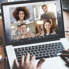 Person typing on a laptop while participating in a video call with four people displayed on the screen.