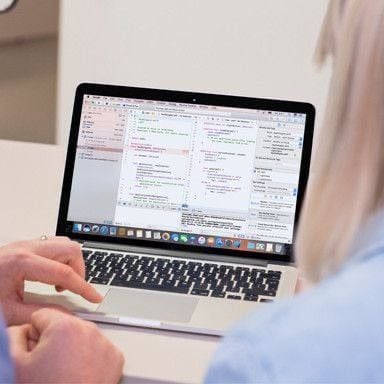 Two people working together on a MacBook laptop.