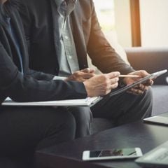 Two people sitting on a couch using a tablet device.