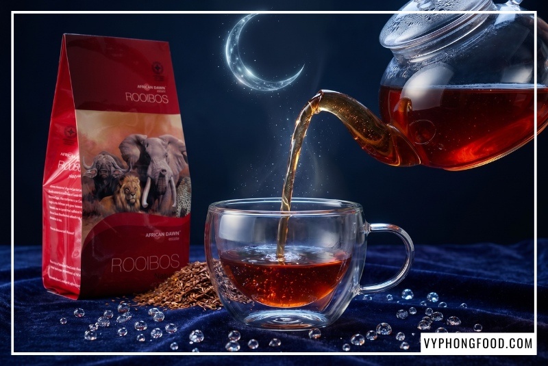 Túi trà rooibos nam phi dạng túi lọc African Dawn đặt cạnh tách trà ấm khói nghi ngút, minh họa giải pháp sử dụng trà thảo mộc không caffeine tự nhiên giúp hạ hormone stress cortisol, cung cấp magie hỗ trợ cơ bắp thư giãn sâu và mang lại giấc ngủ ngon tự nhiên phân phối bởi Vy Phong Food tại veggie.vn.