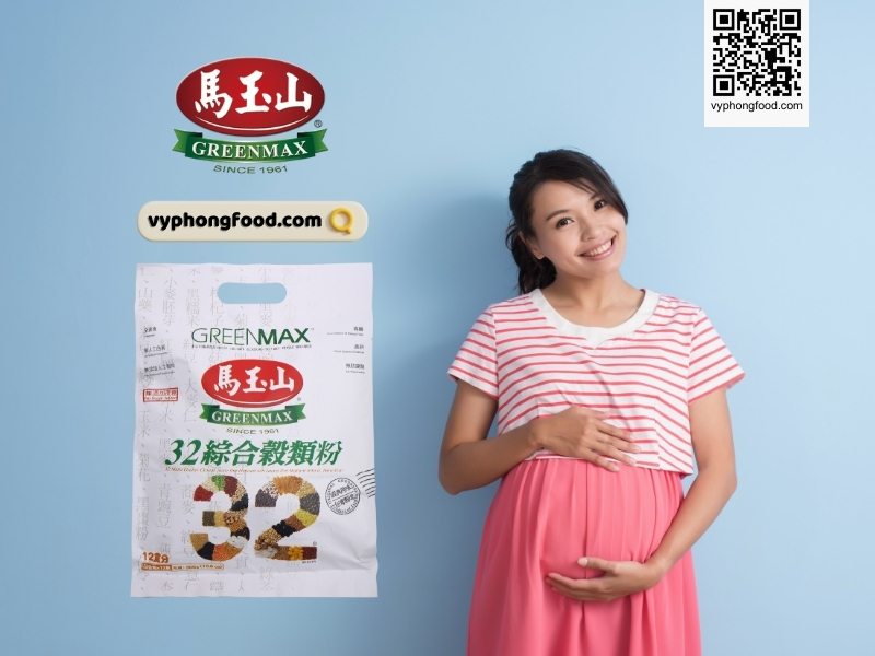 Young pregnant woman sitting at a table reading a prenatal guide about how to drink nutritional cereal powder for pregnant women; Greenmax product guidance and vyphongfood.com branding visible.