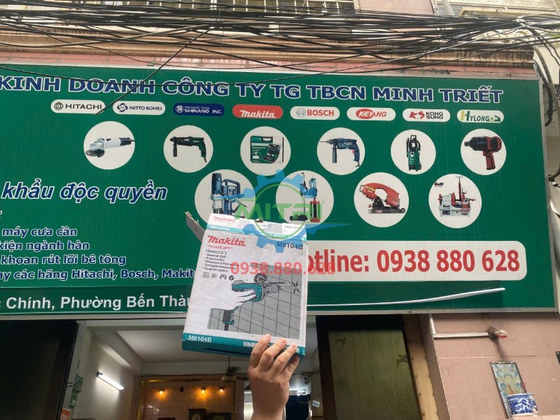 Hộp máy khoan búa Makita M8104B trước bảng hiệu Minh Triết