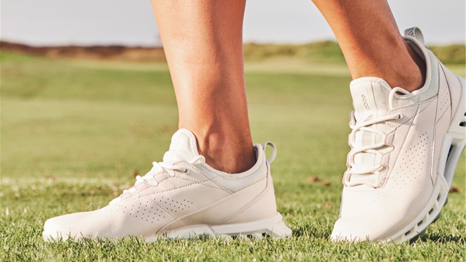 Giày golf trắng buộc dây khi người chơi đứng trên sân cỏ