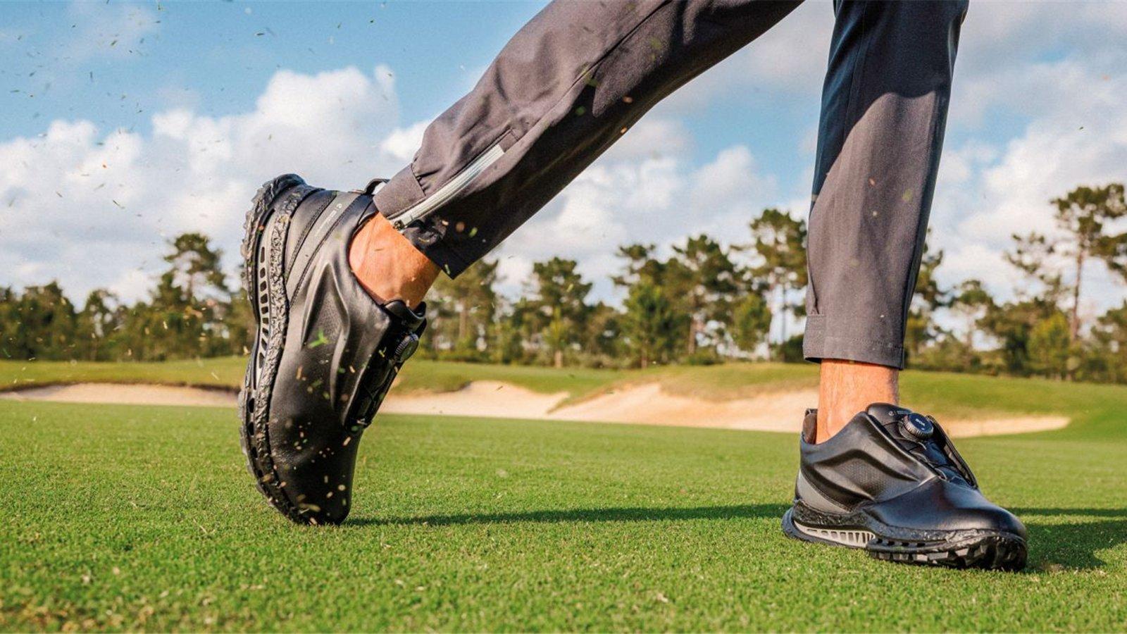 Giày golf ECCO màu đen trên sân cỏ trong động tác chuyển trọng tâm