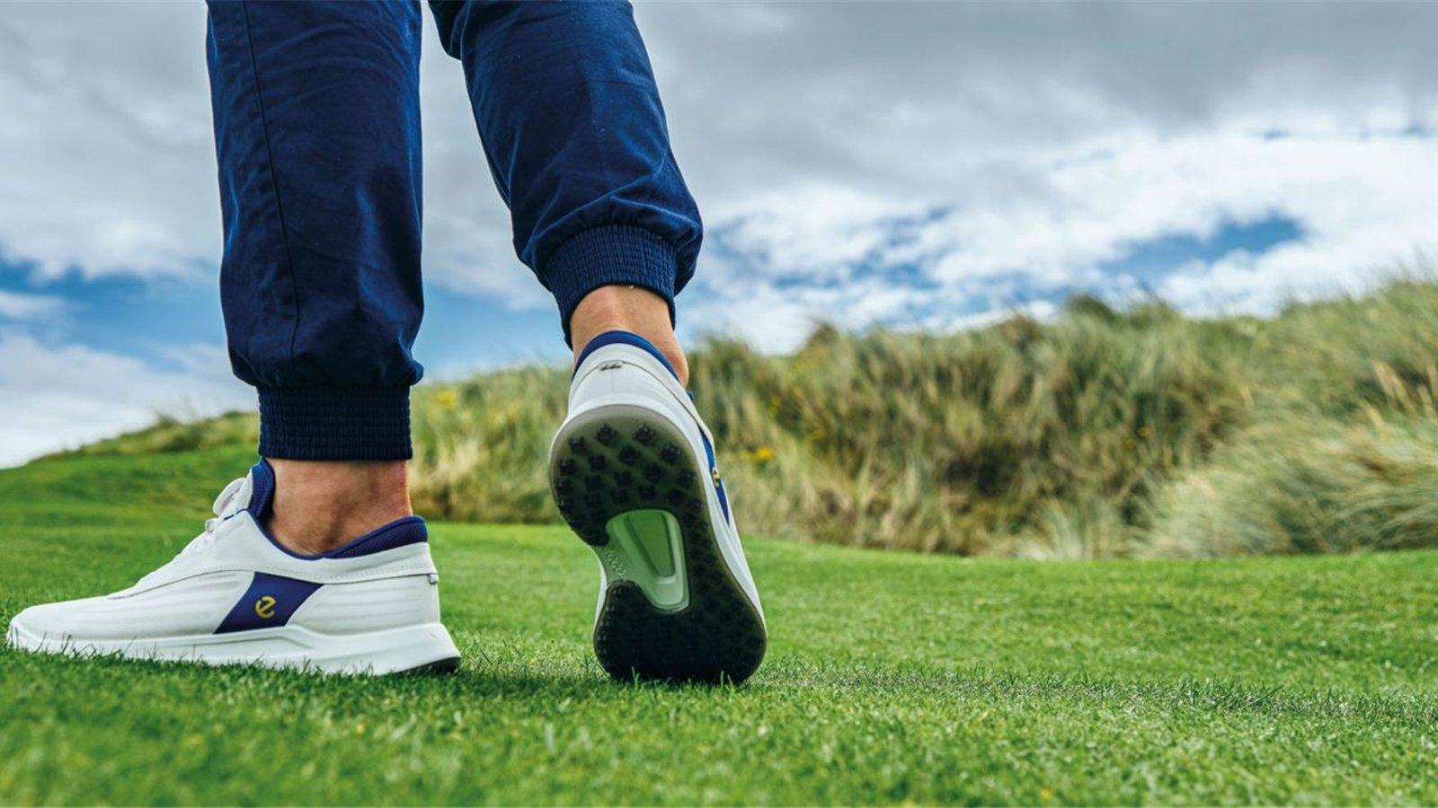 Giày golf trắng phối xanh với đế bám trên sân cỏ