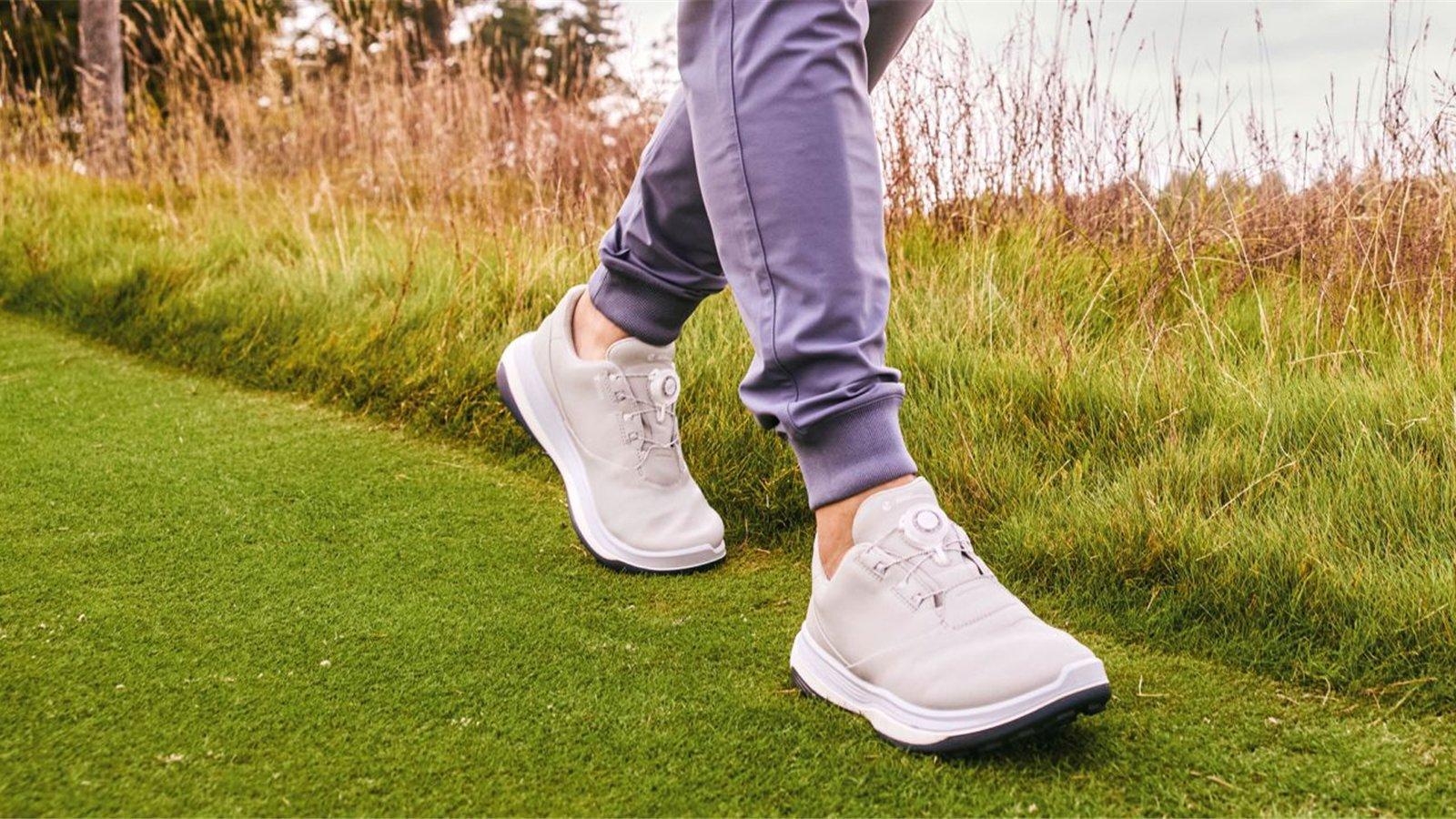 Golfer đi bộ trên sân cỏ với giày golf trắng