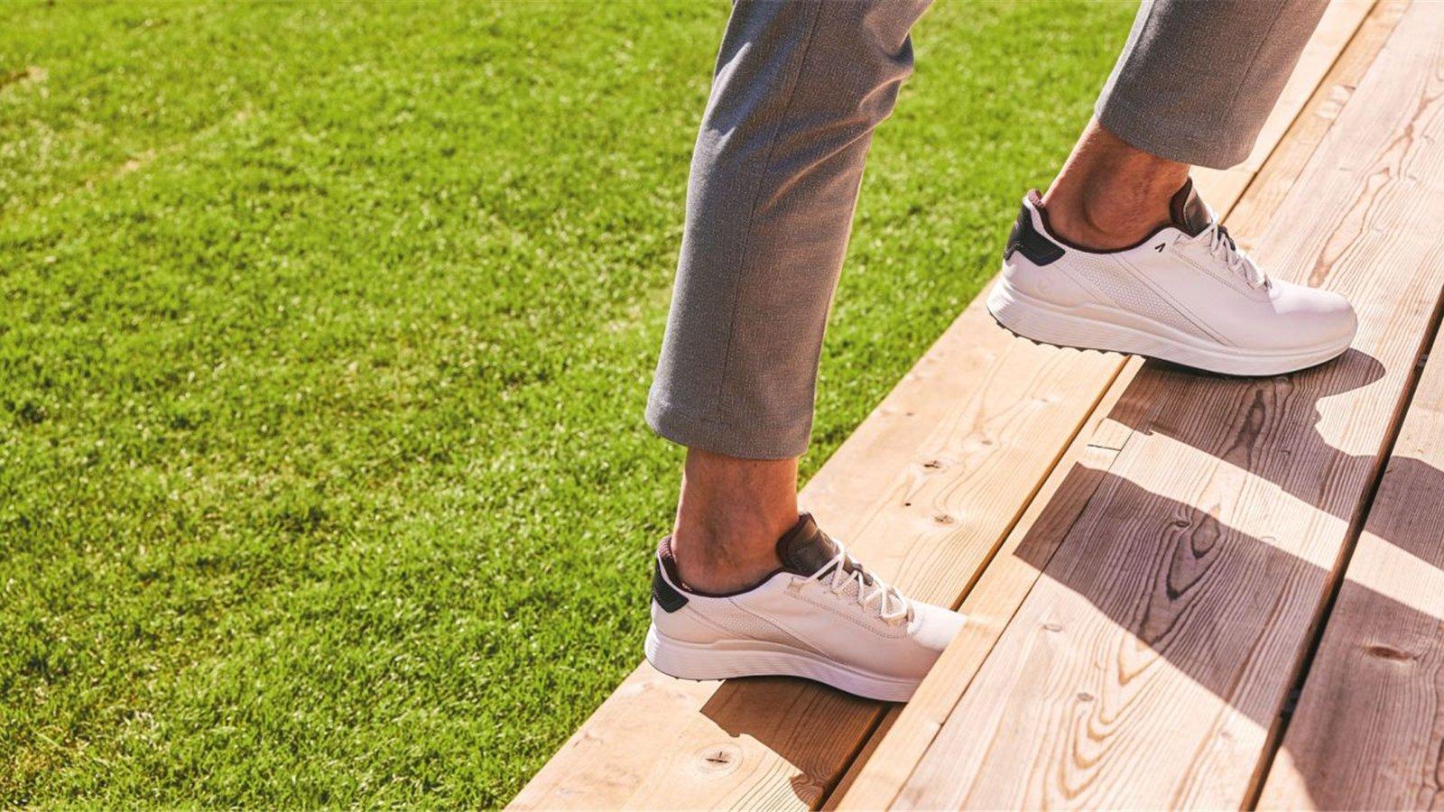 Giày golf trắng trên bậc gỗ cạnh sân cỏ