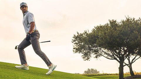 Golfer nam cầm gậy đi trên sân golf lúc chiều muộn