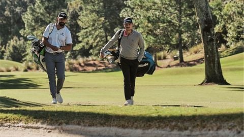 Hai golfer nam mang túi gậy đi bộ trên sân golf