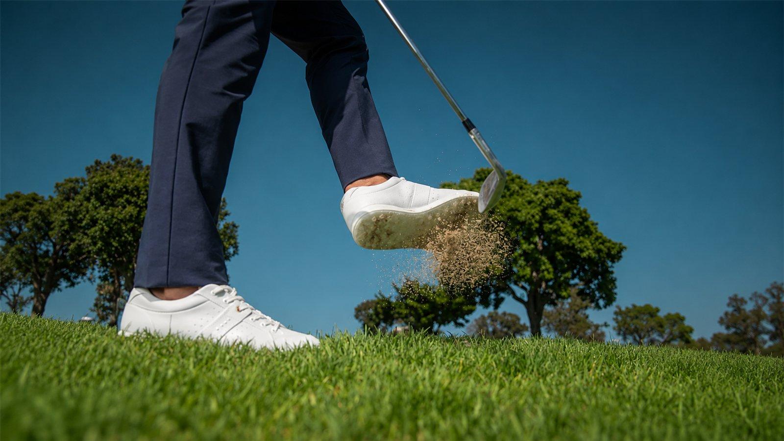 Golfer mang giày golf trắng trên sân cỏ trong cú đánh gậy sắt