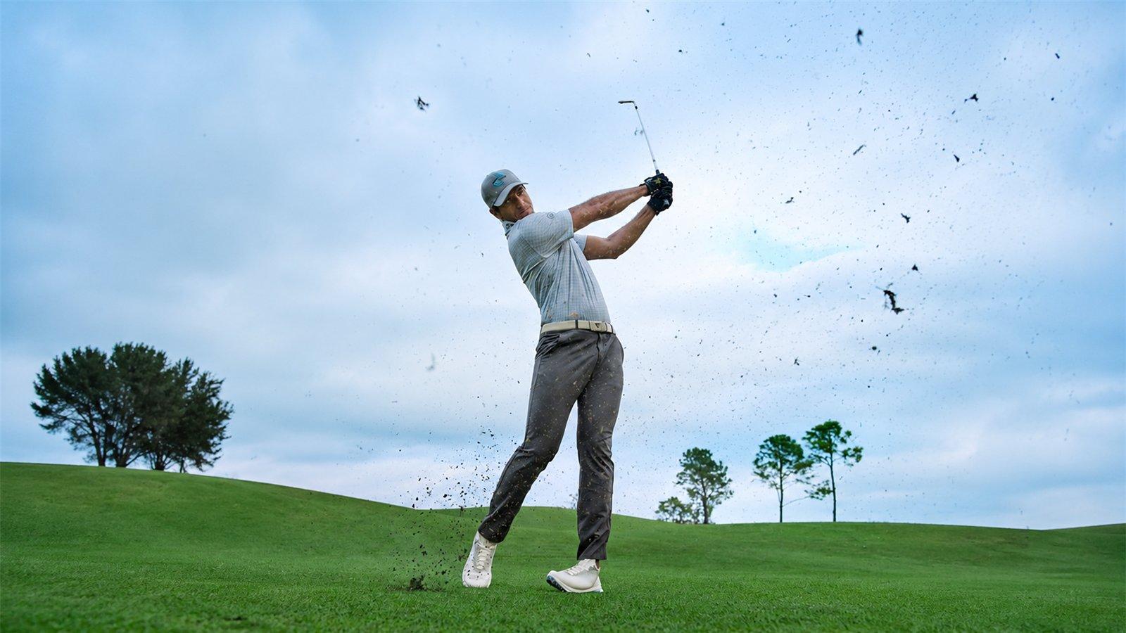 Golfer vung gậy giữa sân cỏ với đất cỏ tung lên