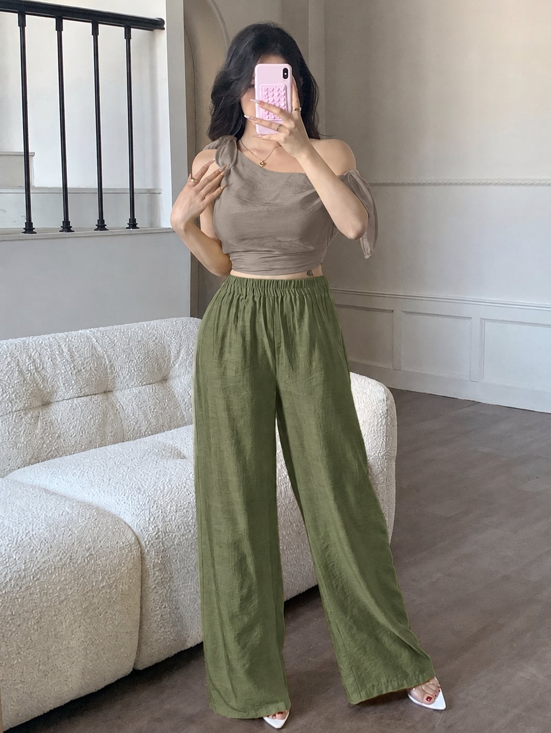 Áo taupe lệch vai phối quần olive trầm, giữ bảng màu tiết chế.