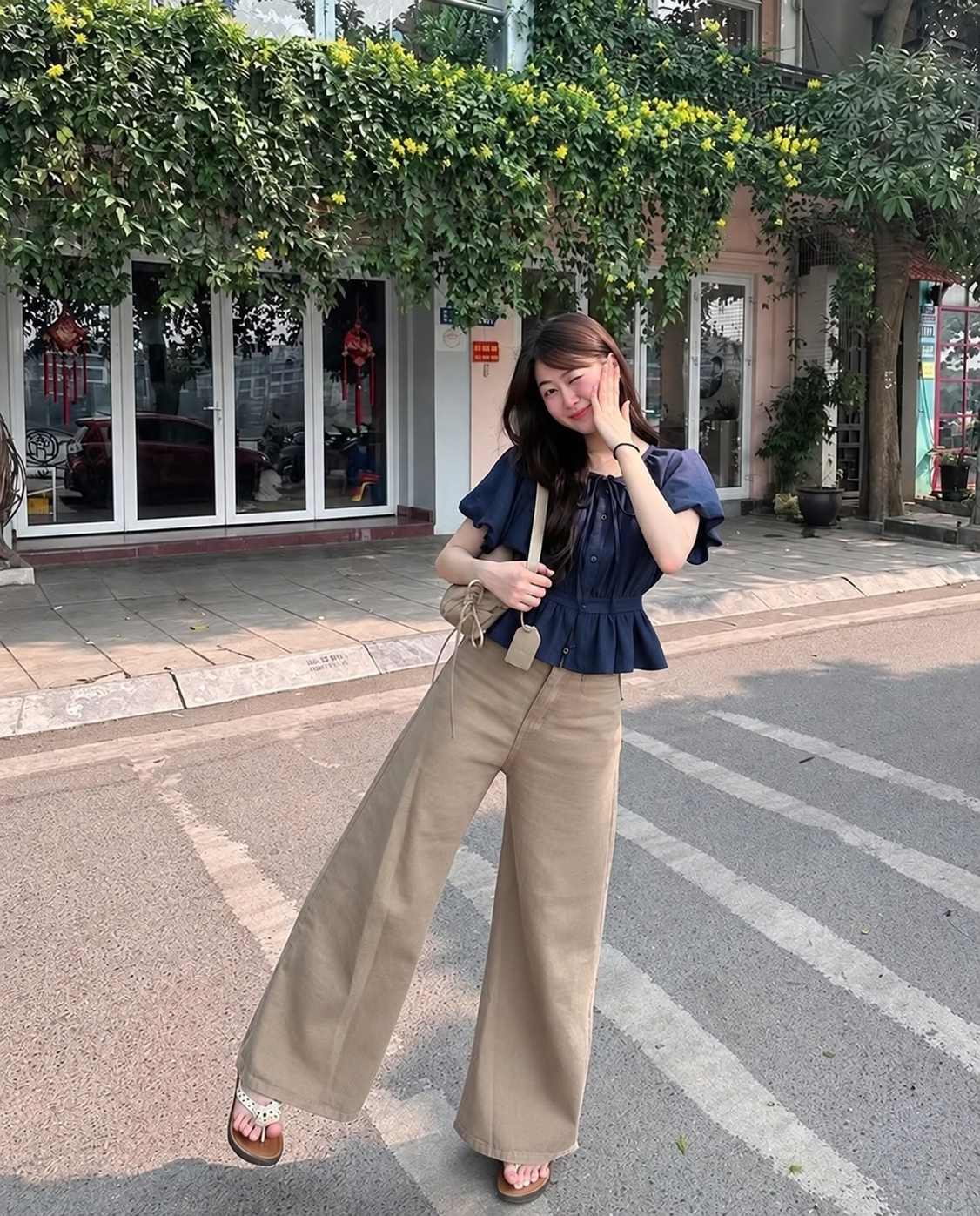 Áo peplum navy tà ngắn xòe nhẹ phối quần ống rộng màu be rủ mềm.