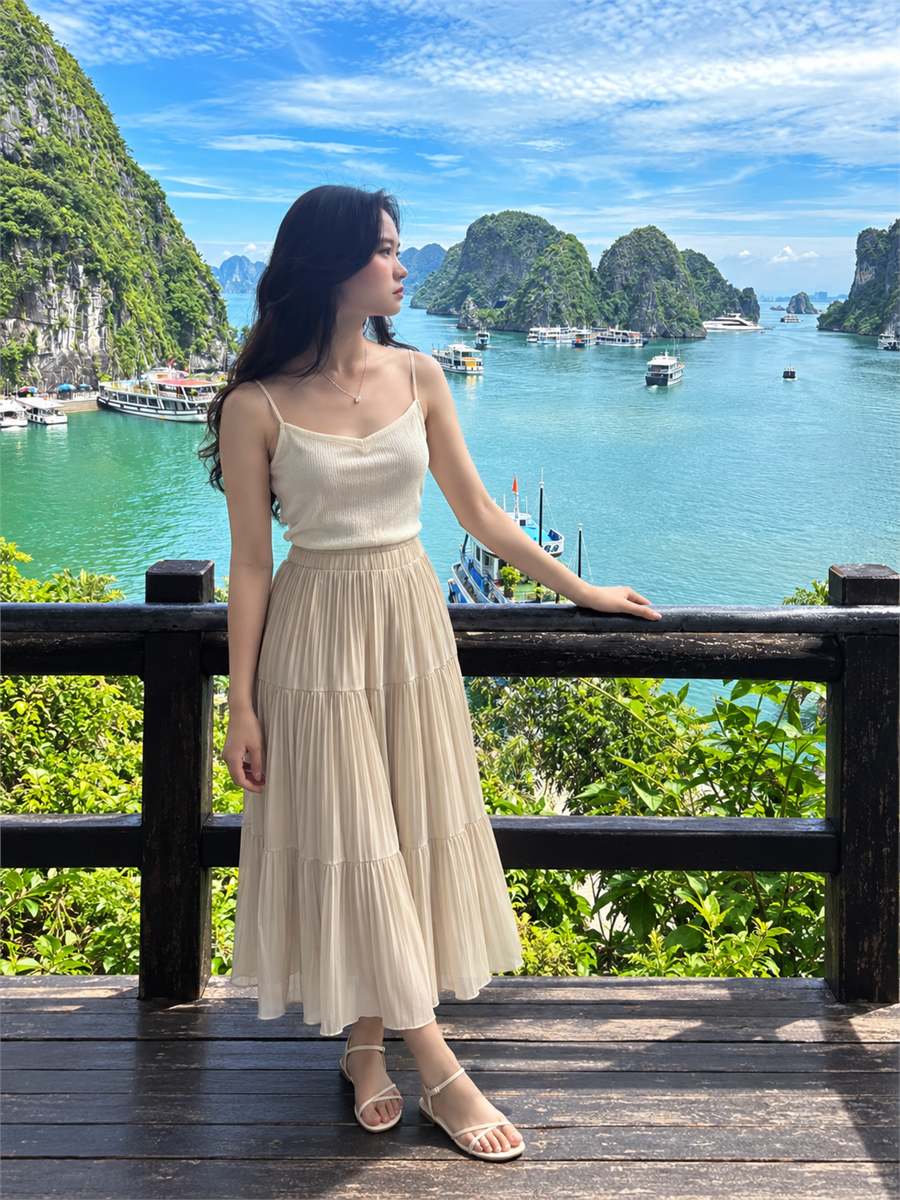Áo hai dây màu kem phối chân váy midi và dép quai hậu trước cảnh vịnh