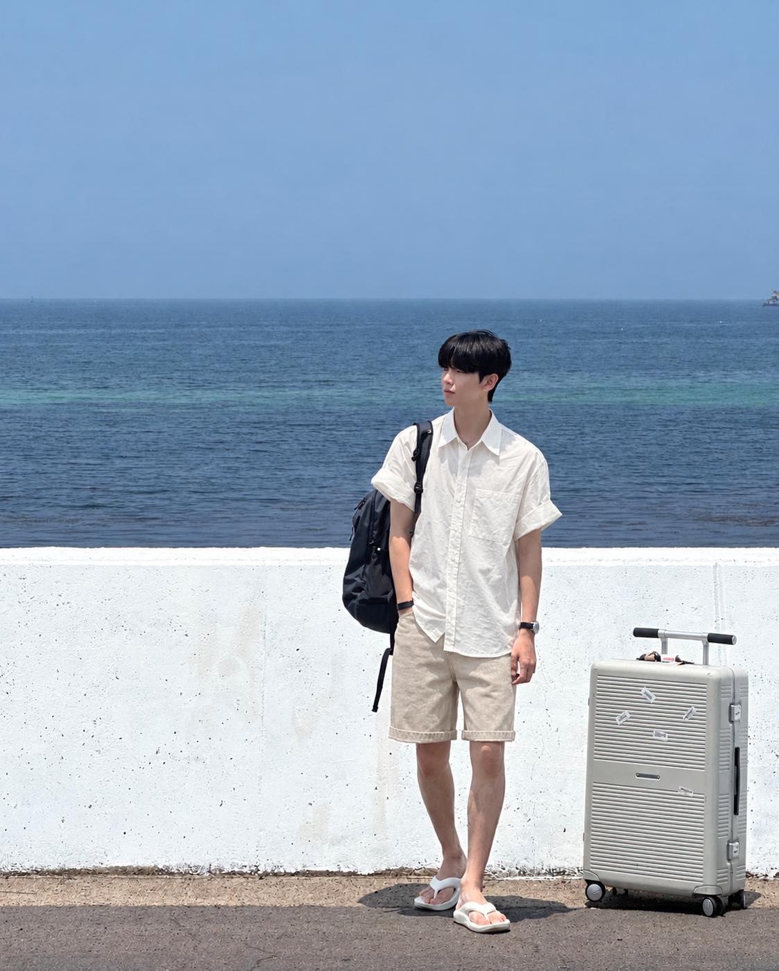 Nam mặc sơ mi linen trắng, quần short màu be và sandal trắng bên bờ biển