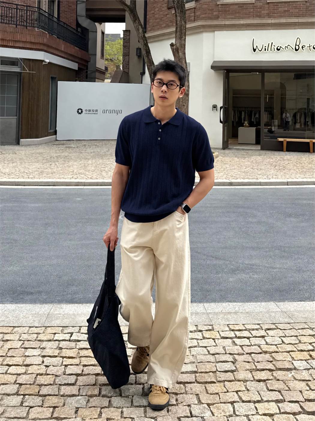 Nam đeo kính phối áo polo xanh navy với quần chinos be và sneaker màu nâu nhạt