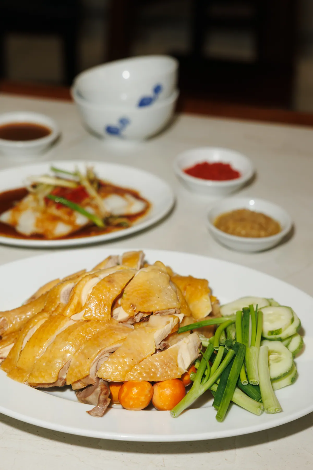 Dĩa gà luộc Đông Nguyên chặt miếng, ăn cùng dưa leo và hành, bày trên bàn với các chén nước chấm