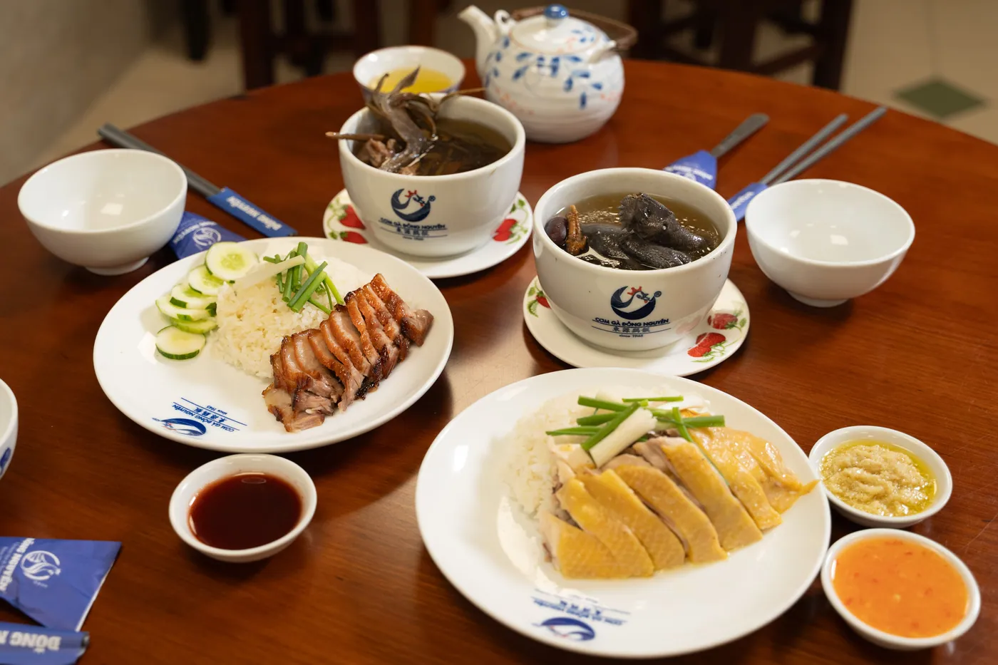 Mâm bàn tròn Chợ Lớn: cơm gà, xá xíu, hai thố canh tiềm và các chén nước chấm