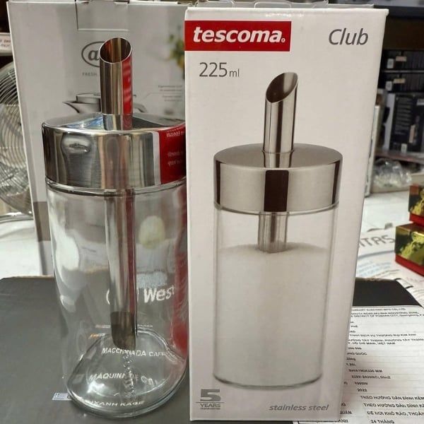Bình đựng đường Tescoma Club 225ml đặt cạnh hộp sản phẩm, chất liệu thép không gỉ sáng bóng.