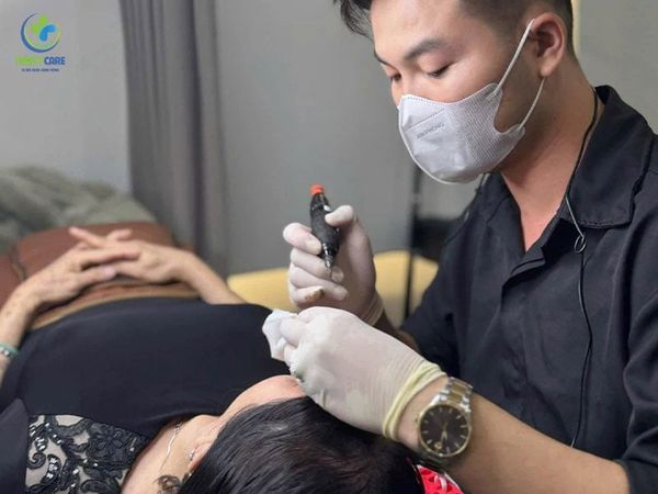 Chuyên viên đang tỉ mỉ thực hiện kỹ thuật đi màu cho khách hàng tại một địa chỉ phun môi hồng cam uy tín.