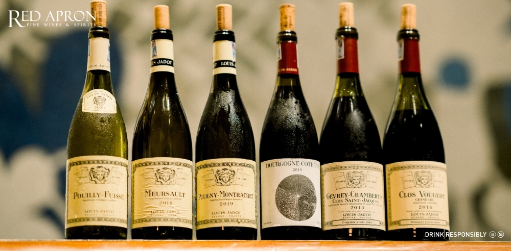 Sáu chai rượu vang Maison Louis Jadot với nhãn và màu sắc khác nhau xếp thành hàng, thể hiện danh mục rượu vang [từ khóa chính] đa dạng từ Beaujolais-Villages đến các cuvée Burgundy cao cấp mà Red Apron phân phối.