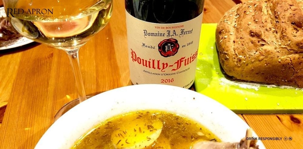Chai rượu Domaine J.A. Ferret Pouilly-Fuissé 2016 đặt cạnh ly vang trắng, bát súp và bánh mì trên bàn gỗ, minh họa cách thưởng thức rượu Maconnais.
