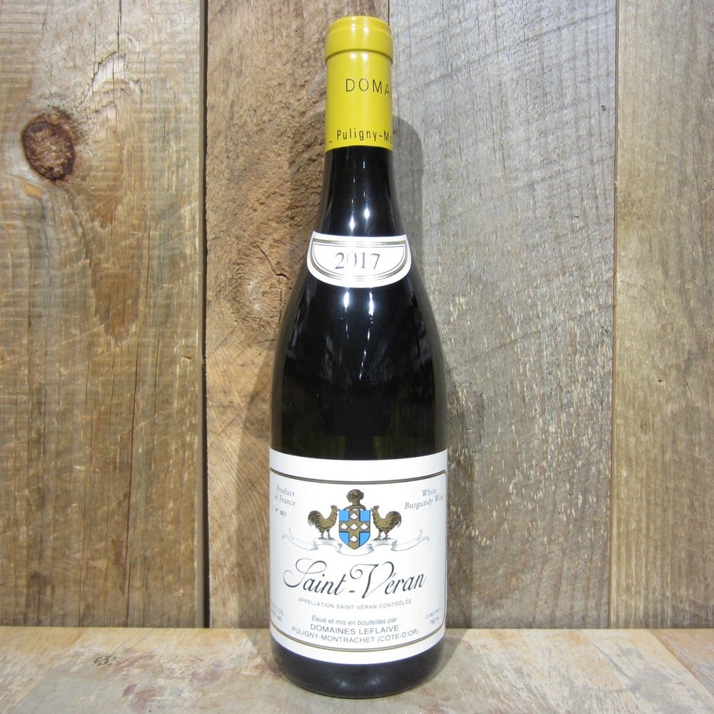 Cận cảnh chai rượu Domaines Leflaive Saint-Véran 2017 với nhãn trắng và cổ chai vàng, đặt trước nền gỗ mộc mạc.
